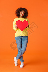 白卡波心头肌全长垂直拍摄可爱 浪漫和可爱的时尚年轻非洲裔美国女性看着相机 拿着大红心卡表达爱意 情人节快乐 表白同情背景