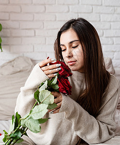 年轻美女坐在床上 庆祝情人节 盛着红玫瑰的晚礼日 假期 微笑背景图片