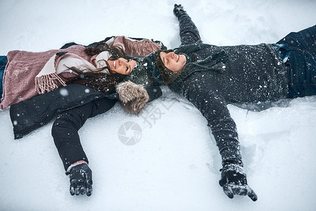 雪让我们再次感觉像孩子一样 一对躺在雪地里的情侣在造雪天使的高角度拍摄背景图片