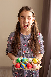 染料盘一个有趣的黑发女孩 穿着衣服 拿着一个装满彩色鸡蛋的纸板盘背景