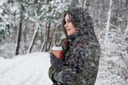 温暖的饮料有助于保持炎热 穿着温暖衣服和咖啡杯咖啡的女孩在冬季森林中散步图片
