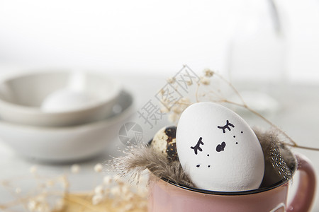 复活节概念 一个白蛋 有铜丝耳朵和在杯子上涂漆的兔子睡脸 帕崔奇鸡蛋和羽毛 装饰风格 填料背景图片