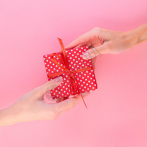 礼从天降两个女人拿着礼物放在一个带蝴蝶结的红色礼盒里 把它从一个人传给另一个人背景