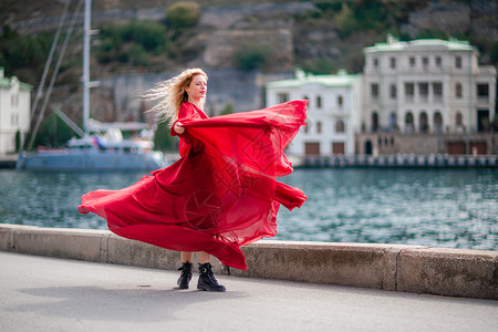 柳岩红裙飞舞身着红裙的女子 长着丝绸长翅膀的时装模特 身着飘逸的裙子 在堤岸上飞舞着布料 女孩 长的背景