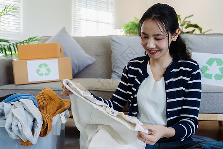 亚洲女性从旧衣服箱中挑选衣服进行回收 回收服装概念图片