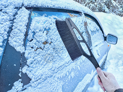 冬日清晨汽车除雪。寒冷的冬日清晨，女人用手扫去车上的积雪图片