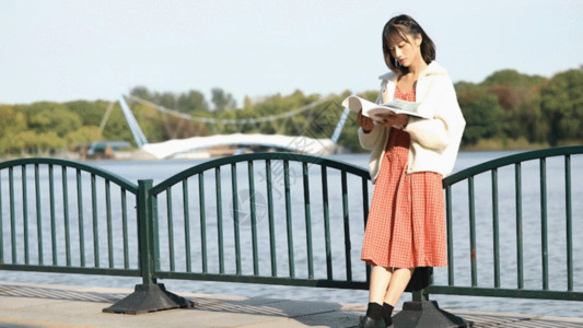 拿手机展示的青年女性文艺少女户外湖边看书GIF高清图片