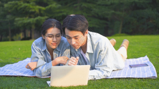 在电脑前讨论的青年夫妻大学生在草地上使用电脑学习GIF高清图片