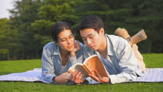 看书休闲情侣在草坪上趴着看书GIF高清图片