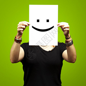 女人在绿色背景下在脸前展示一张带笑容表情的白纸图片