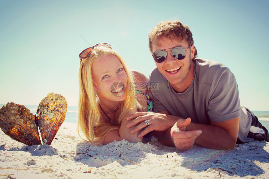 一个有吸引力的快乐年轻夫妇躺在海边的海滩上微笑着图片