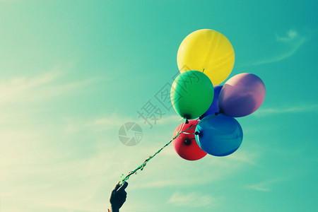天空背景上手中彩色气球的特写图片