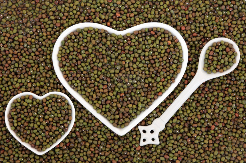 心形瓷盘和瓷勺中的绿豆形成抽象背景图片