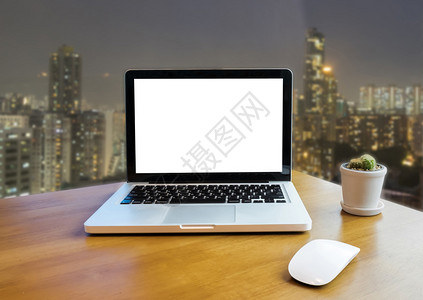 办公室桌上和夜间建筑的笔记本电脑前端背景图片
