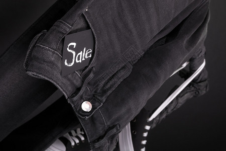 黑色牛仔裤紧贴着牌子Sale挂在黑背景的衣架上图片