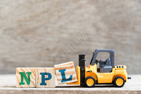 在木材背景上用NPL字不履行贷款非专利文学的减缩表示Toy叉车图片