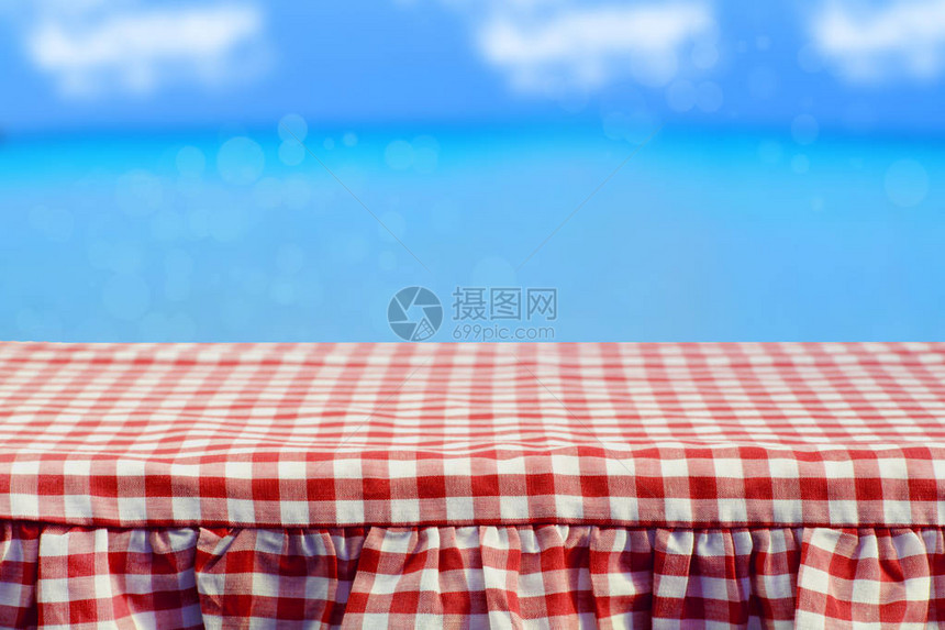 空木甲板桌与抽象明亮的蓝天和云彩背景上的红色方格桌布为您的食物和产图片