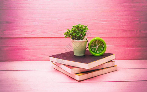堆叠成烟幕木板的书时钟和陶瓷锅以及粉红木板上的植物的抽象图片