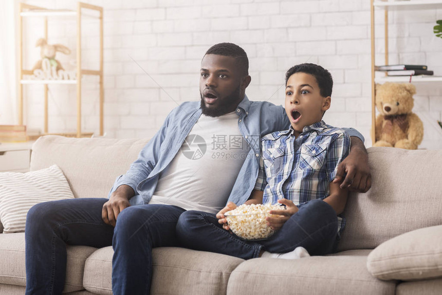 震惊的黑人父亲和少年儿子在家电视上看动作电影图片