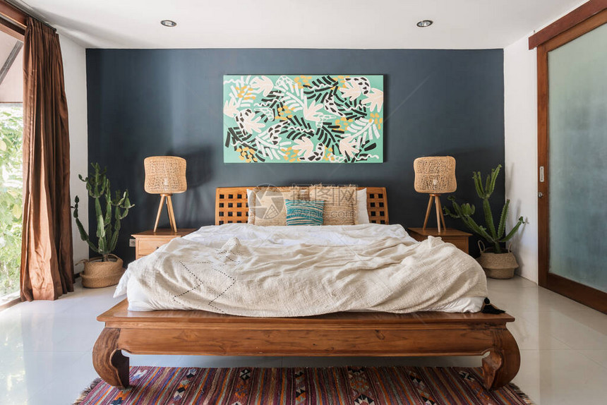 舒适房屋的经典室内卧室拥有民族装饰木制床头柜上的灯舒适的床地板上的编织装饰地毯墙上的绘画和篮子里的异图片