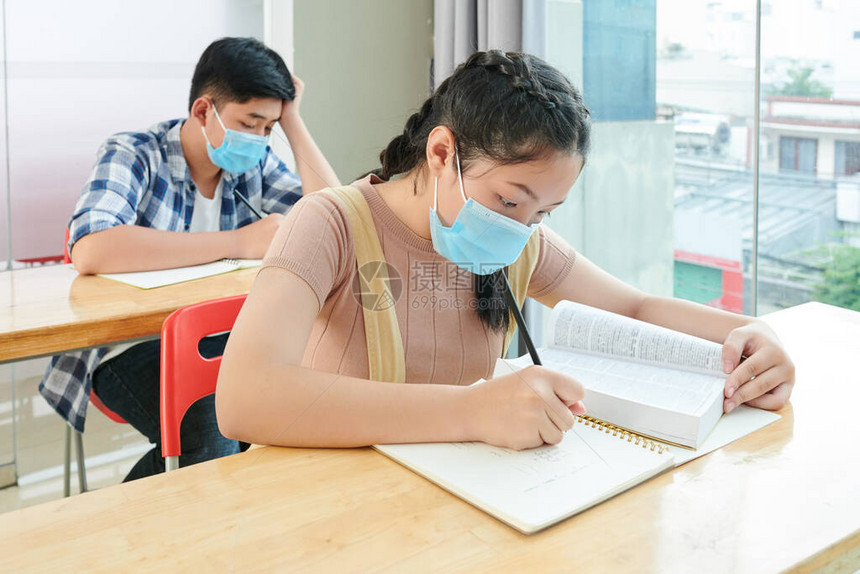 戴着医用口罩的越南学童在上课时看书和写字图片