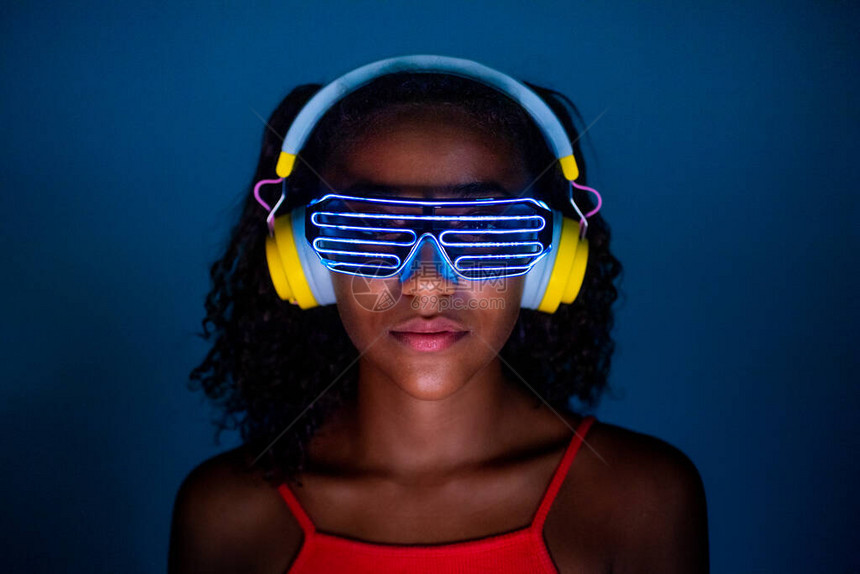 蓝色背景中戴耳机和未来派LED眼镜的年轻女图片