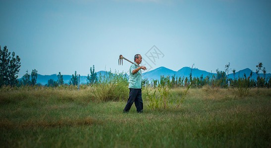 清晨农夫扛着锄头在山下开荒种植背景图片