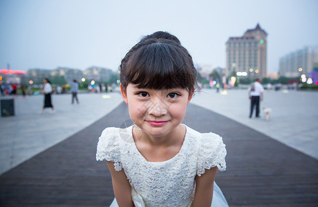 傍晚小姑娘穿着白裙站在广场上露出特殊的表情高清图片