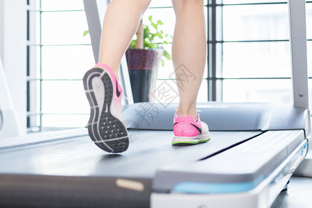 趴在跑步机上休息喝水的健身女性健身房跑步机运动跑步脚步特写背景