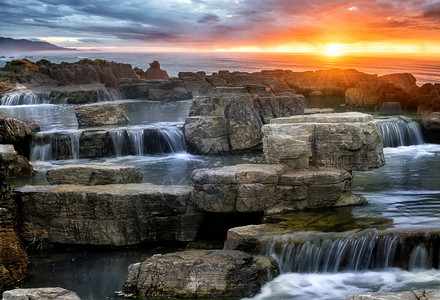 阳光下的海边的石头和瀑布背景图片