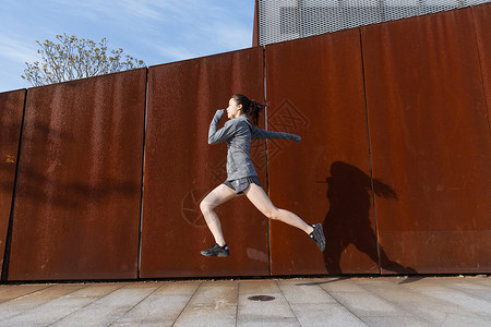 运动女孩在生锈铁板前跳跃背景图片