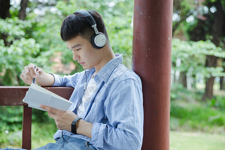 耳机男帅气大学生坐在凉亭听音乐看书背景