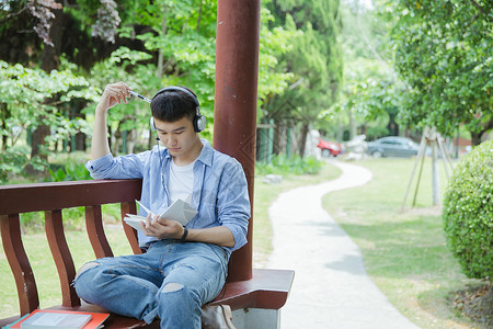 帅气大学生坐在凉亭听音乐看书高清图片