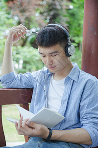 帅气大学生坐在凉亭听音乐看书图片