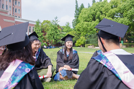 坐男穿学士服毕业大学生坐草地聊天背景