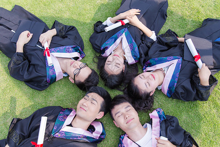 男孩与学士服毕业季大学生们躺草地拿着证书背景