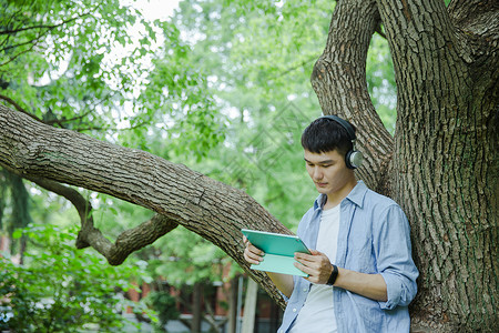 浇树的男孩帅气大学生在用平板电脑听音乐背景