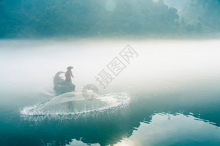 渔夫在起雾的江中撒网打鱼高清图片
