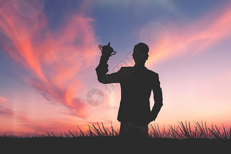 男人身影夕阳下手扶奖杯的成功男人设计图片