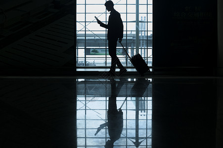 机场门口商务男士手提拉杆箱经过机场一边看着手机背景