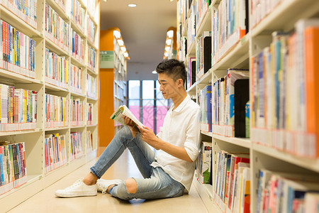 坐着读书男生坐在图书馆书架旁看书的男生背景