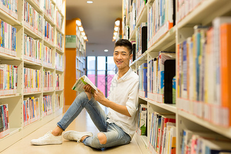坐着看书的老师坐在图书馆书架旁看书的男生背景