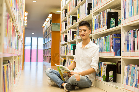 坐着读书男孩坐在图书馆书架旁看书的男生背景