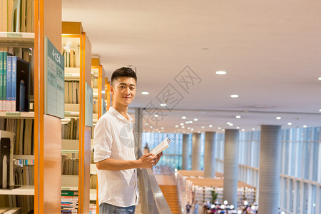 站在图书馆书架旁看书的帅气男同学高清图片