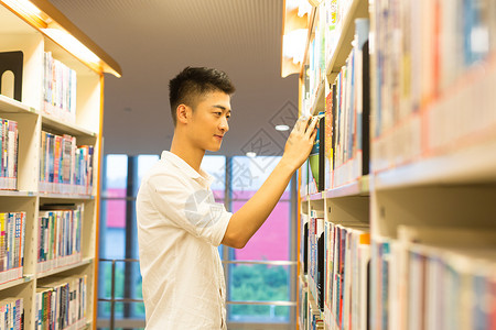 男生在图书馆书架旁选看图书背景图片