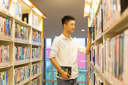 男生在图书馆书架旁选看图书背景图片