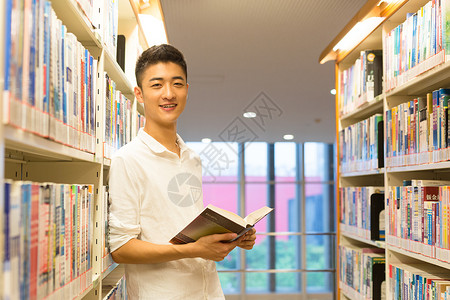 站在图书馆书架旁看书的帅气男高中生图片