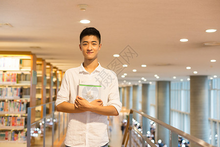 拿书的老师站在图书馆书架旁看书的帅气男同学背景