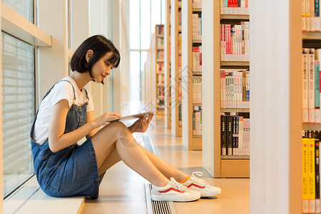 可爱女生鞋坐在图书馆书架旁看书的可爱女生背景