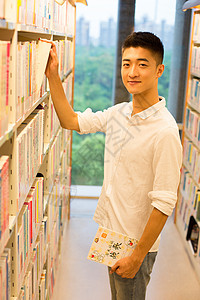 男生在图书馆书架旁选看图书背景图片
